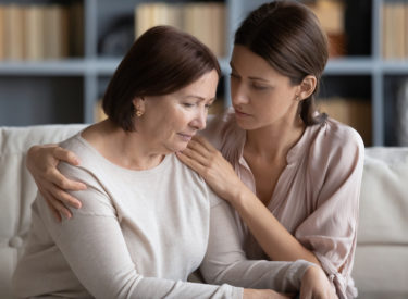 Compassionate woman embracing shoulder of mother